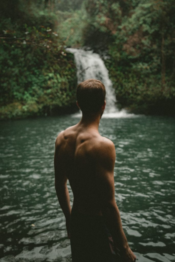 Muscular man facing a waterfall