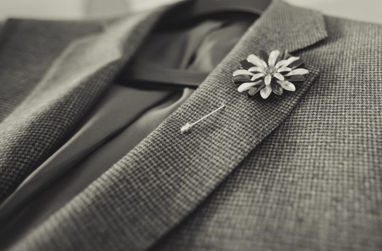 A floral lapel pin on a gray suit.