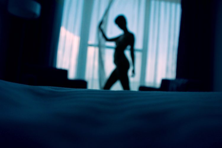 A silhouette of a naked woman standing by the curtain.